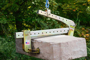 Concrete block with a metal clamp attached, hanging from a rope against a green leafy background.