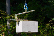 Cement block being lifted by a crane with a blurred green background